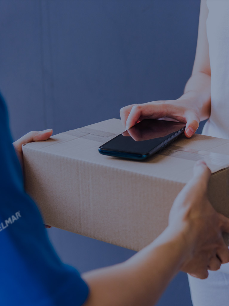 Un homme d'affaires tenant un stylo et un téléphone portable, devant un ordinateur portable ouvert, avec un caddie miniature sur le bureau.