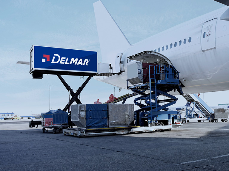 Delmar shipping containers being loaded into the fuselage of an airplane while sitting on an airport tarmac.